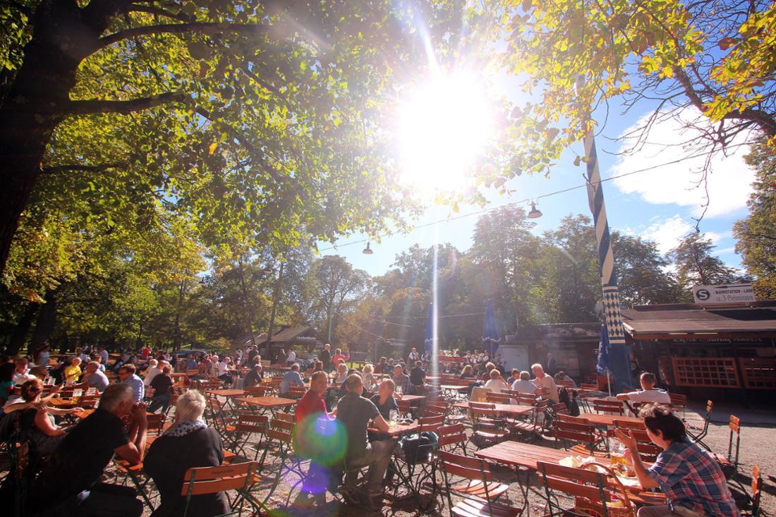Sonnendurchfluteter Biergarten mit Gästen unter Bäumen als Beispiel für alltägliche UV-Belastung